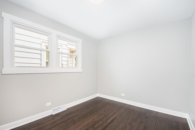 empty room featuring visible vents, baseboards, and dark wood finished floors