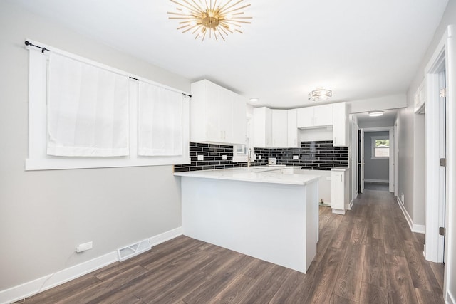 kitchen featuring a peninsula, dark wood-style flooring, visible vents, baseboards, and backsplash