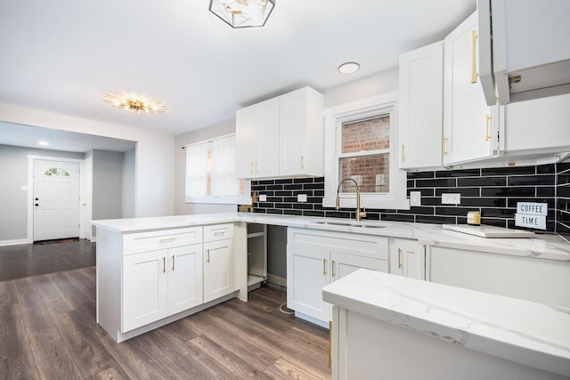 kitchen with dark wood finished floors, decorative backsplash, white cabinets, a sink, and a peninsula