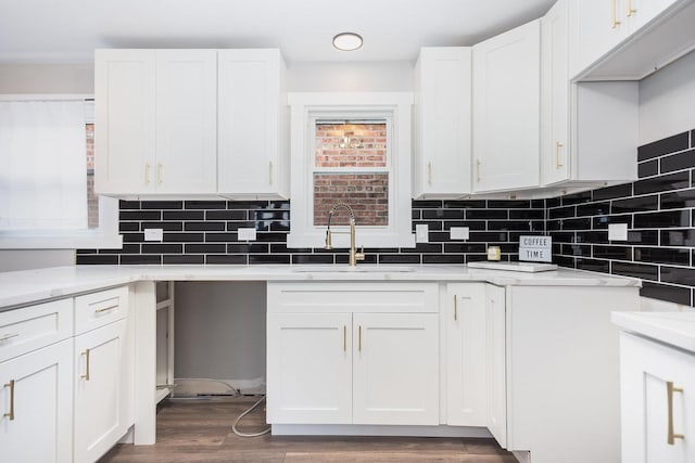 kitchen with white cabinets, dark wood-style flooring, a sink, light stone countertops, and backsplash