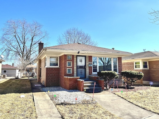 bungalow-style home with brick siding, a chimney, a front yard, and fence