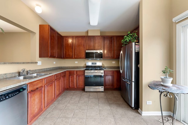 kitchen with baseboards, appliances with stainless steel finishes, light countertops, a sink, and light tile patterned flooring