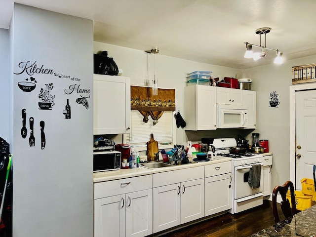 kitchen featuring white appliances, white cabinets, dark wood-type flooring, hanging light fixtures, and a sink