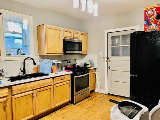 kitchen with pendant lighting, stainless steel appliances, light countertops, a sink, and light wood-type flooring