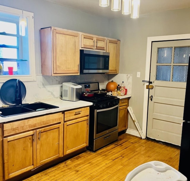 kitchen with light wood-style flooring, appliances with stainless steel finishes, decorative light fixtures, light countertops, and a sink