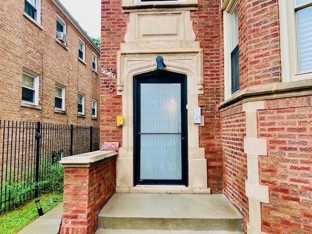 property entrance featuring fence, cooling unit, and brick siding