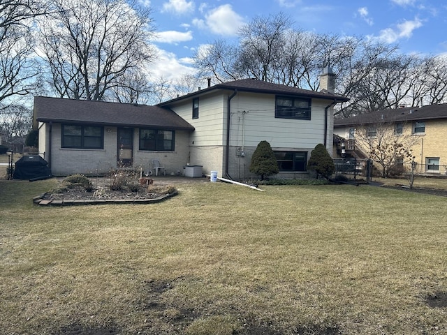 back of house with brick siding, a lawn, a chimney, and fence