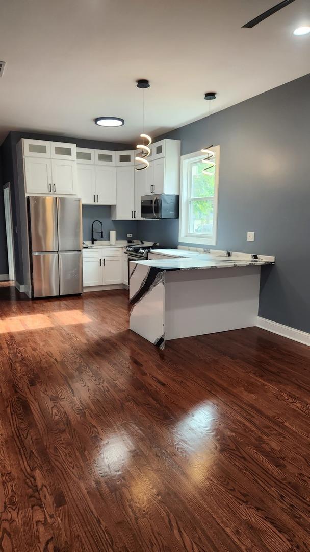 kitchen featuring pendant lighting, appliances with stainless steel finishes, glass insert cabinets, dark wood-type flooring, and white cabinetry