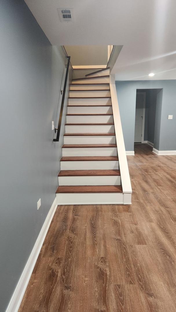 staircase featuring wood finished floors, visible vents, and baseboards