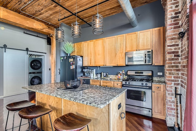 kitchen featuring a barn door, stacked washer / dryer, wood ceiling, appliances with stainless steel finishes, and beamed ceiling