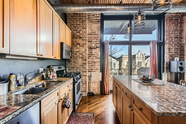 kitchen with wood finished floors, brick wall, appliances with stainless steel finishes, and a sink