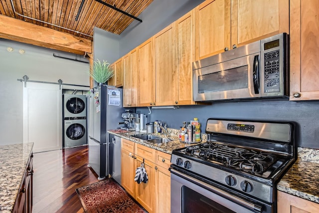 kitchen with a barn door, wooden ceiling, a sink, stacked washer / drying machine, and appliances with stainless steel finishes