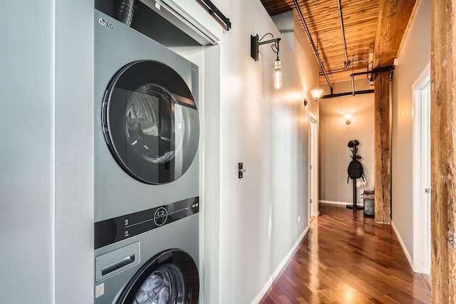 clothes washing area featuring stacked washer and dryer, laundry area, wood finished floors, wood ceiling, and baseboards