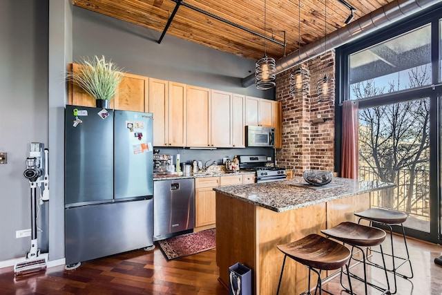 kitchen featuring dark stone countertops, dark wood-type flooring, stainless steel appliances, light brown cabinetry, and a kitchen bar