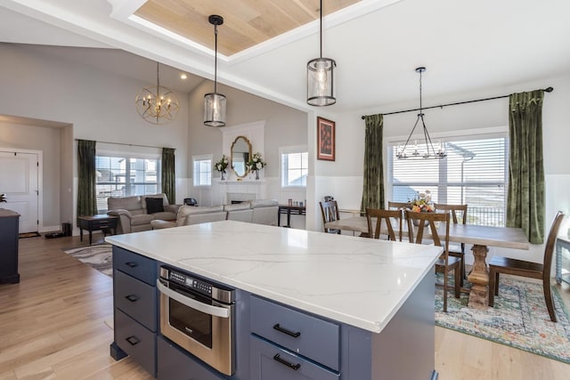 kitchen with a notable chandelier, a wainscoted wall, light stone countertops, light wood finished floors, and decorative light fixtures