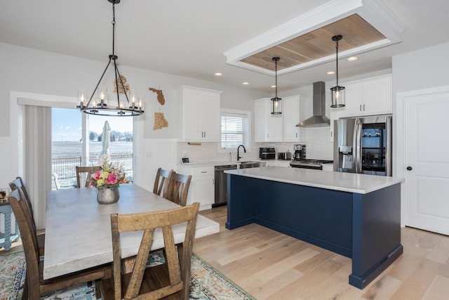 kitchen with stainless steel appliances, light countertops, light wood-style flooring, and wall chimney exhaust hood