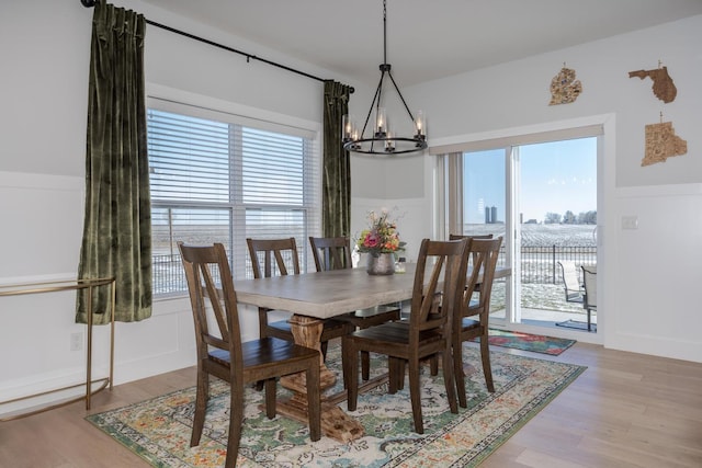 dining area with an inviting chandelier, light wood-style flooring, a decorative wall, and wainscoting