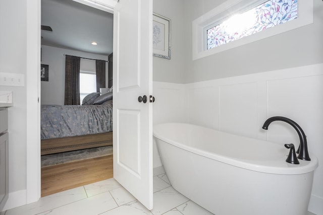 ensuite bathroom featuring marble finish floor, a wainscoted wall, a freestanding bath, and ensuite bath