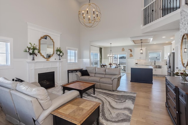 living room featuring a chandelier, a wealth of natural light, a wainscoted wall, and light wood finished floors