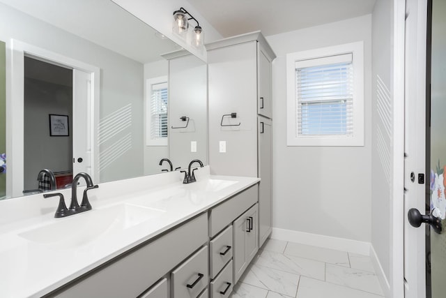 bathroom with marble finish floor, a sink, baseboards, and double vanity