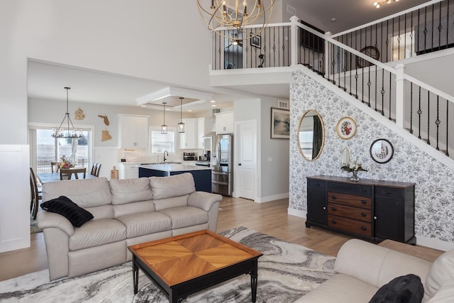 living area featuring baseboards, a towering ceiling, stairway, an inviting chandelier, and light wood-type flooring