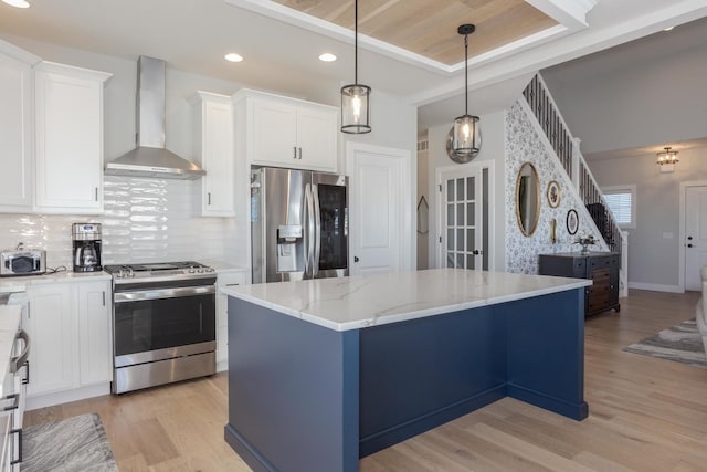 kitchen with decorative backsplash, wall chimney exhaust hood, a kitchen island, appliances with stainless steel finishes, and light wood-style floors