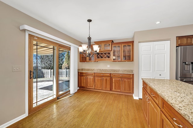 kitchen with glass insert cabinets, light wood-style flooring, stainless steel refrigerator with ice dispenser, brown cabinets, and decorative light fixtures