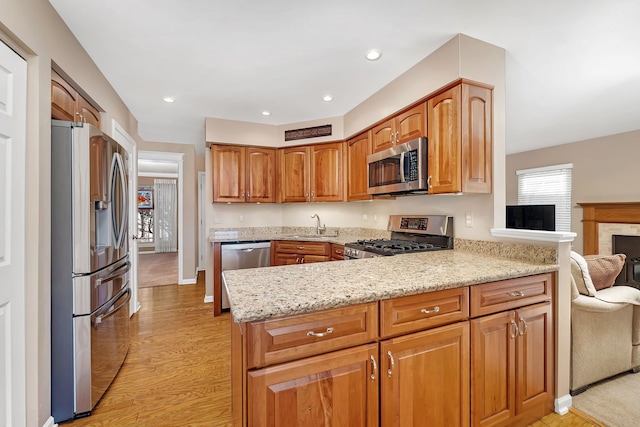 kitchen with light stone counters, stainless steel appliances, a peninsula, a sink, and light wood-type flooring