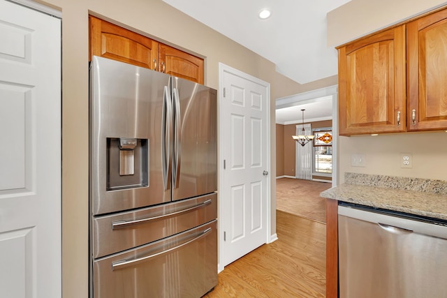 kitchen with light wood finished floors, brown cabinetry, appliances with stainless steel finishes, light stone countertops, and crown molding