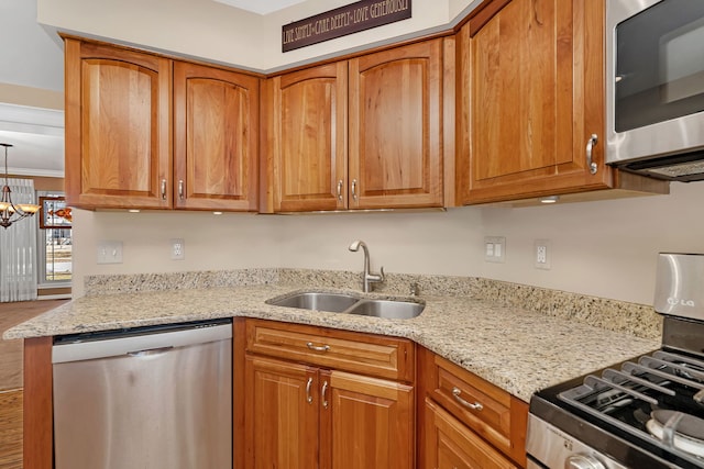 kitchen with appliances with stainless steel finishes, brown cabinetry, a sink, and light stone counters