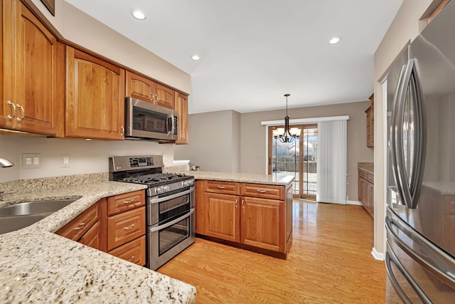 kitchen with stainless steel appliances, a peninsula, a sink, light wood-style floors, and brown cabinets