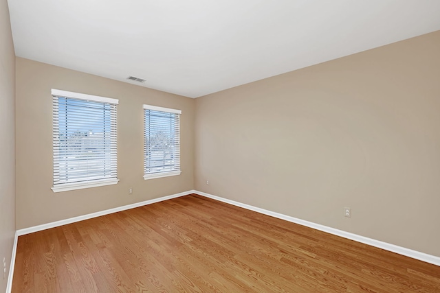 empty room with baseboards, visible vents, and wood finished floors