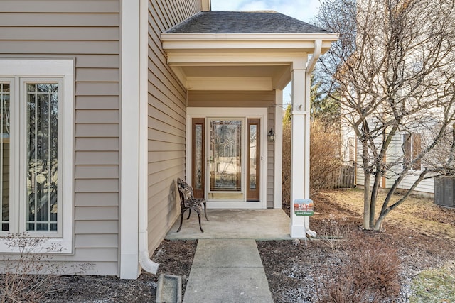 entrance to property featuring a shingled roof, central AC unit, and fence