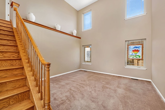 staircase with a high ceiling, carpet flooring, visible vents, and baseboards