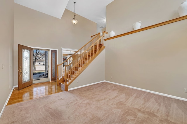 foyer featuring baseboards, stairs, a high ceiling, and carpet flooring