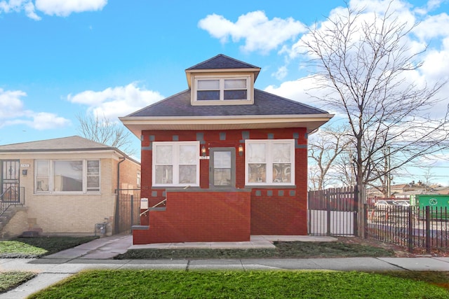 bungalow featuring a shingled roof, brick siding, and fence