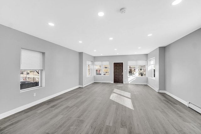 unfurnished living room featuring baseboard heating, baseboards, and wood finished floors