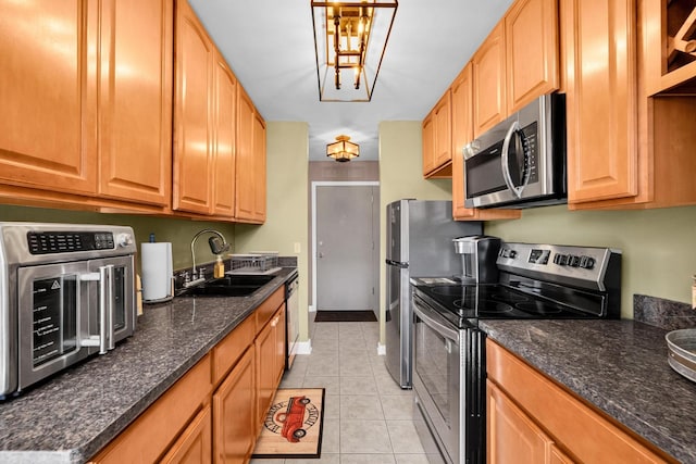 kitchen featuring light tile patterned floors, stainless steel appliances, a sink, dark stone counters, and baseboards