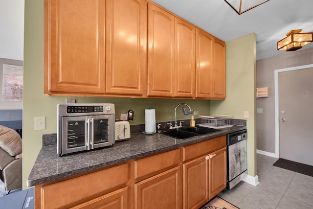 kitchen featuring light tile patterned floors, a sink, dark stone countertops, dishwasher, and baseboards