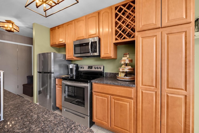 kitchen with light tile patterned floors, appliances with stainless steel finishes, and dark stone countertops