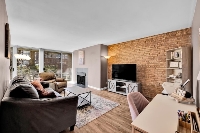 living area featuring brick wall, a fireplace with flush hearth, baseboards, light wood-type flooring, and floor to ceiling windows