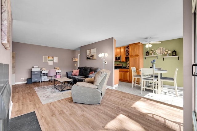 living area with a ceiling fan, light wood-type flooring, and baseboards