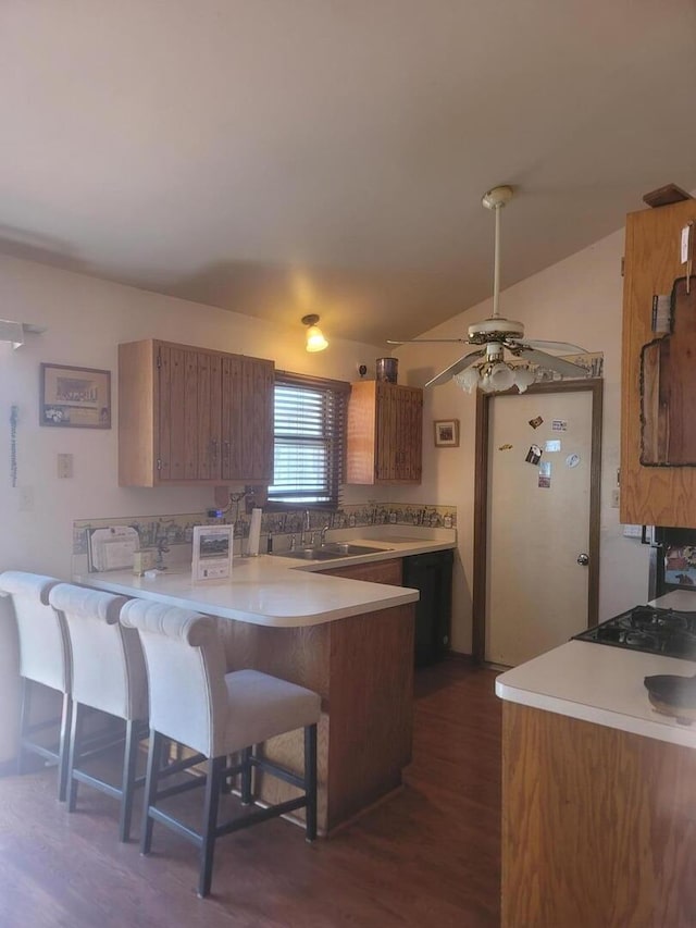 kitchen with a peninsula, a kitchen breakfast bar, light countertops, brown cabinets, and dark wood finished floors