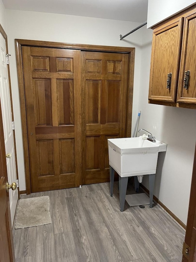 clothes washing area with baseboards, cabinet space, and light wood finished floors