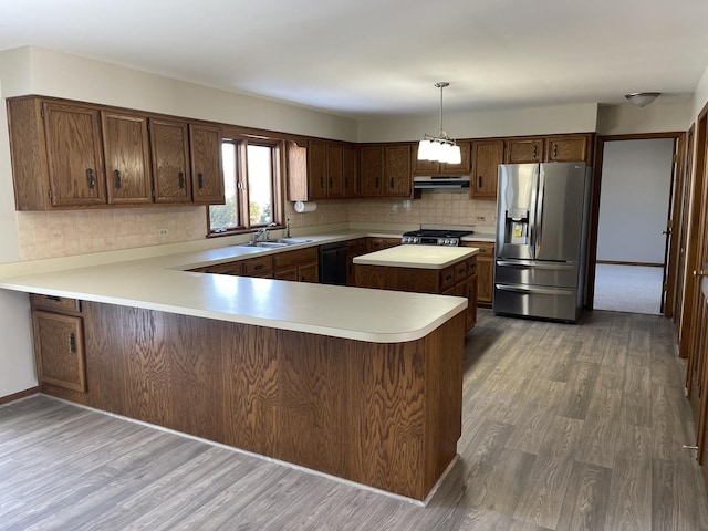 kitchen with under cabinet range hood, stainless steel appliances, wood finished floors, light countertops, and backsplash