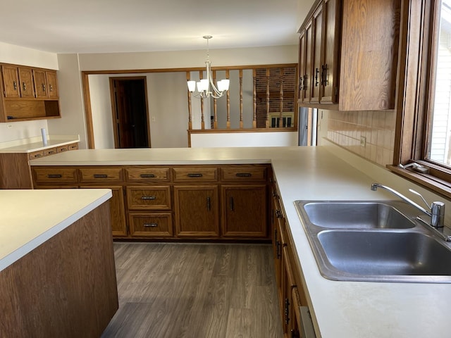 kitchen with dark wood-style flooring, decorative light fixtures, a peninsula, light countertops, and a sink