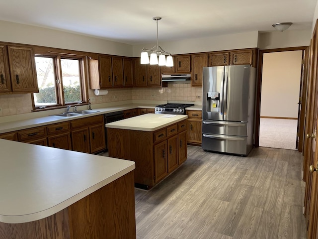 kitchen with a sink, stainless steel appliances, light countertops, under cabinet range hood, and backsplash