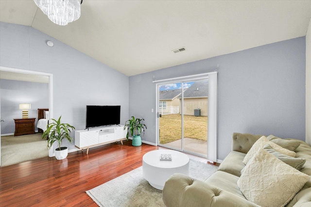 living room with wood finished floors, visible vents, baseboards, an inviting chandelier, and vaulted ceiling