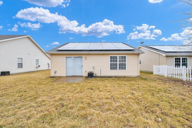 back of house with solar panels, a yard, fence, and central AC