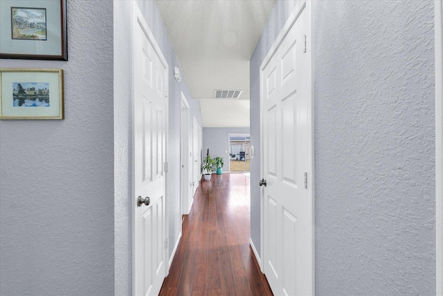 corridor with dark wood-style flooring and a textured wall